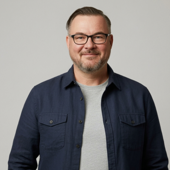 Smiling man with glasses, short beard, wearing a casual dark jacket and light grey shirt.